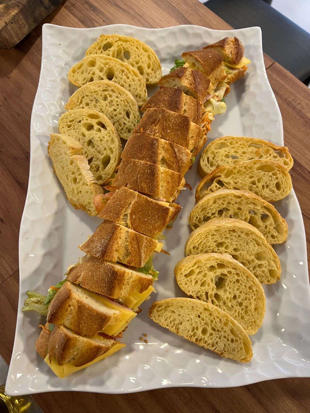 Um prato branco coberto com fatias de pão e sanduíches em uma mesa de madeira.
