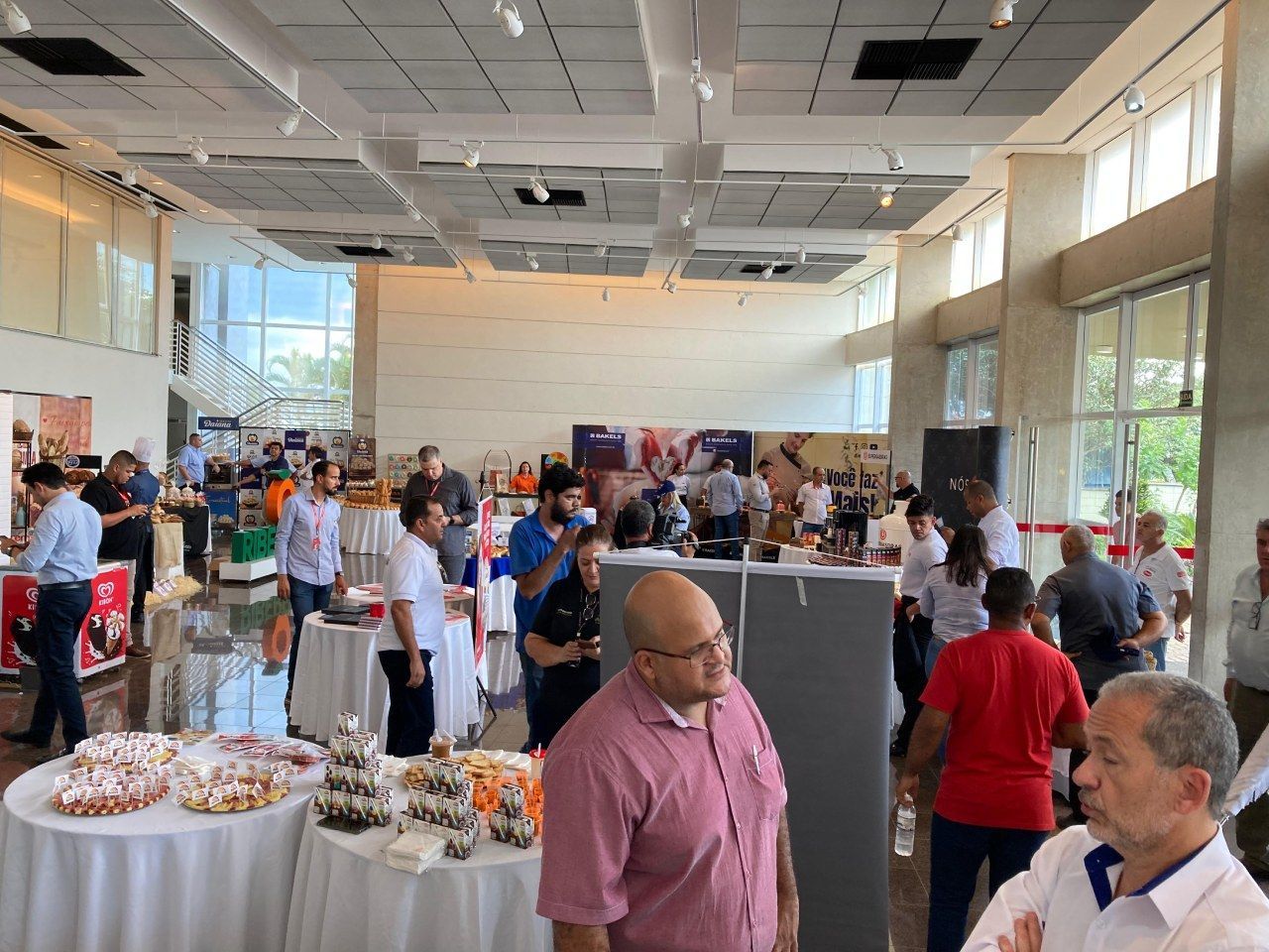 Um grupo de pessoas está em volta de mesas em uma grande sala.