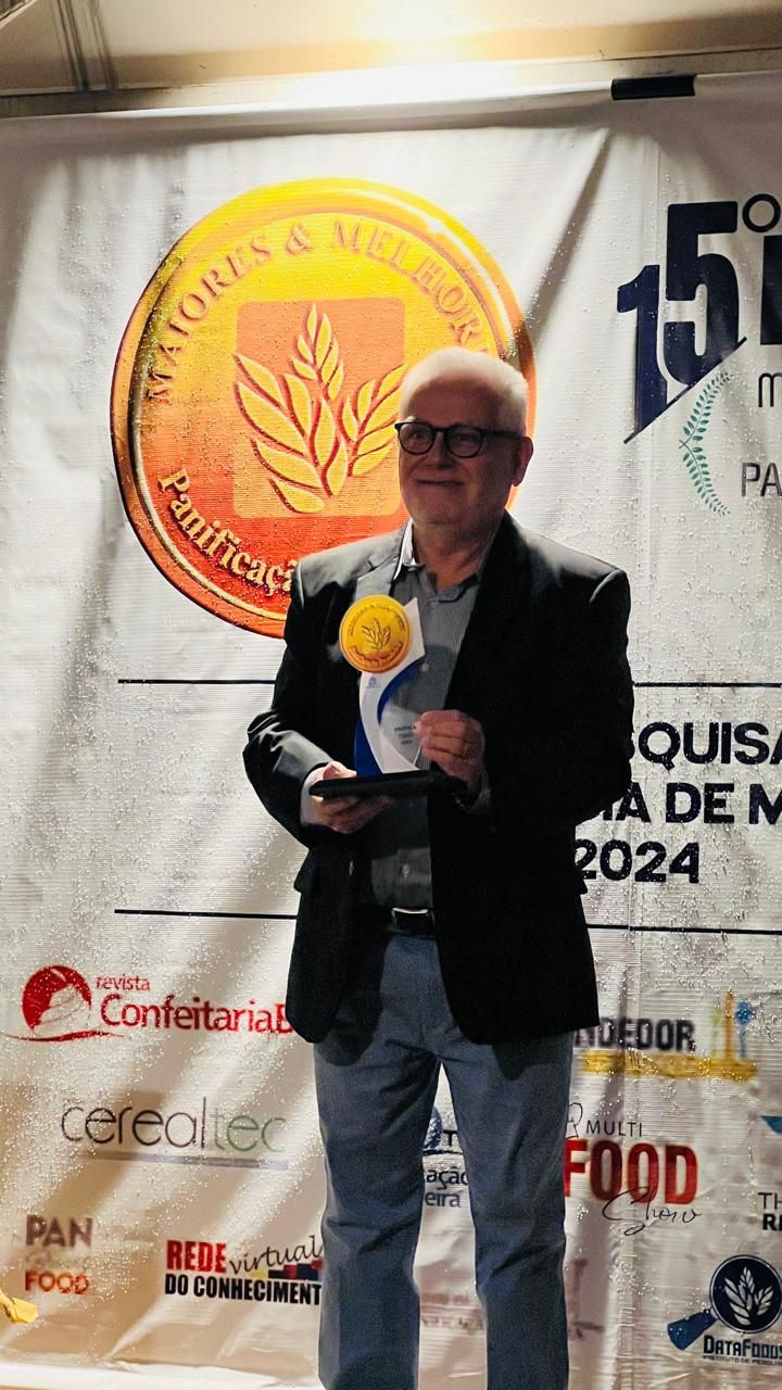 Um homem de terno segura um troféu em frente a uma faixa.