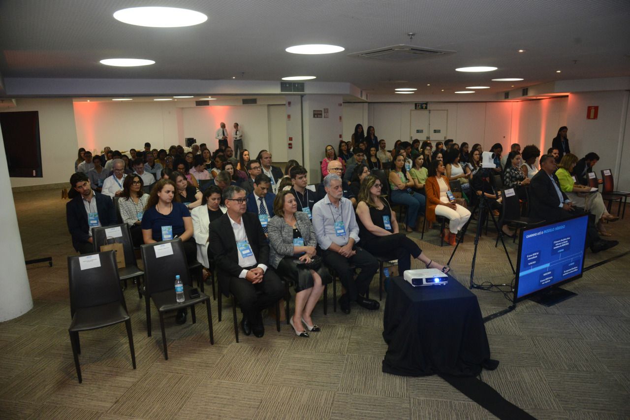 Um grande grupo de pessoas está sentado em uma sala assistindo a uma apresentação.
