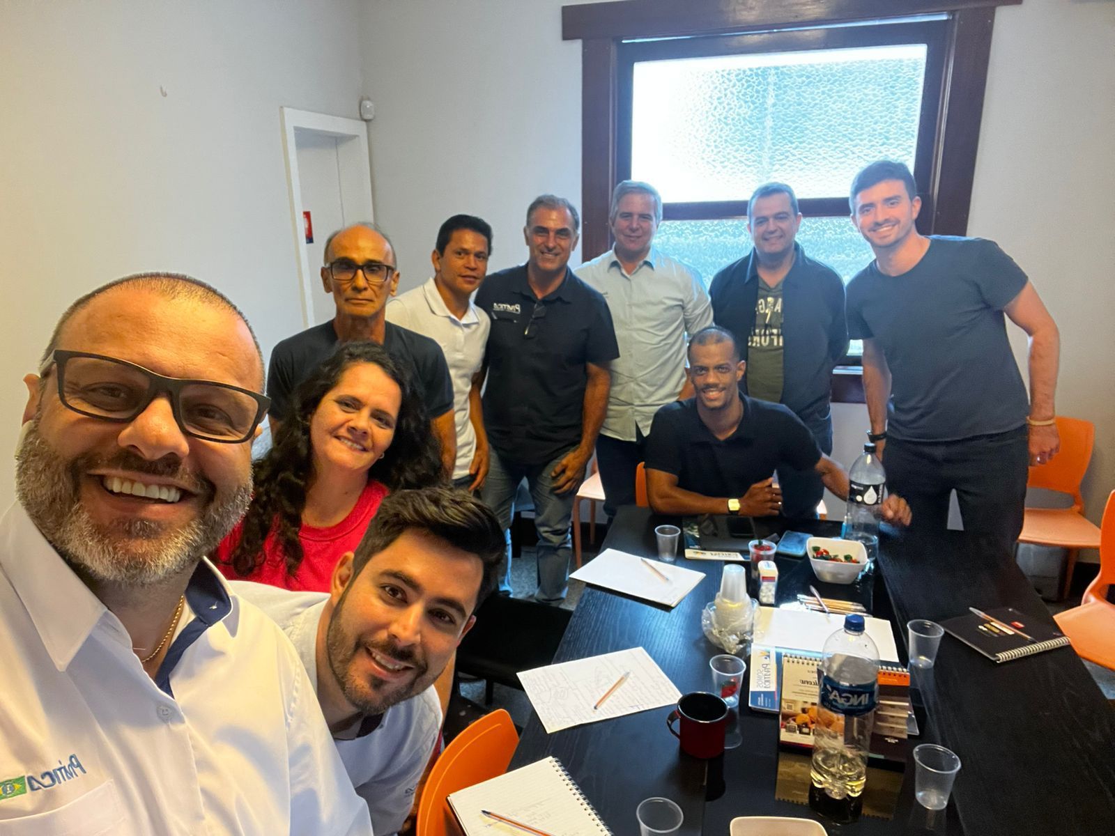 Um grupo de pessoas está posando para uma foto sentadas ao redor de uma mesa.