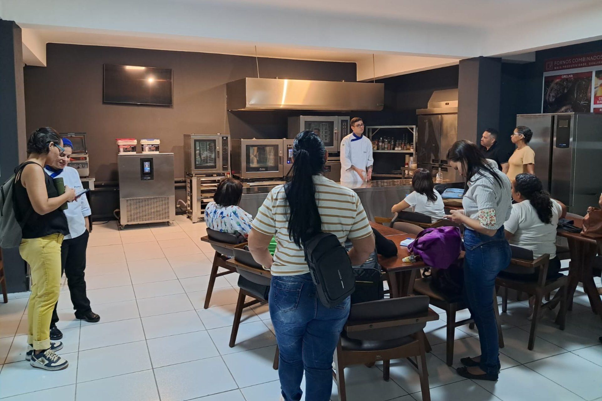 Um grupo de pessoas está em pé ao redor de uma mesa na cozinha.