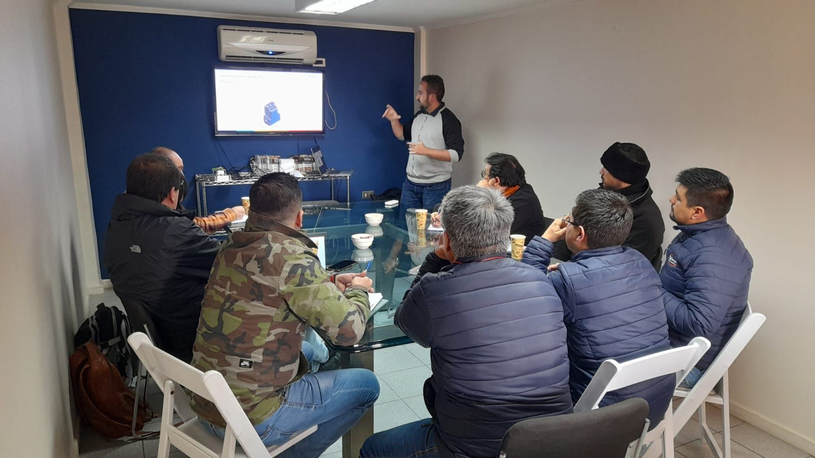 Um homem está fazendo uma apresentação para um grupo de homens sentados ao redor de uma mesa.