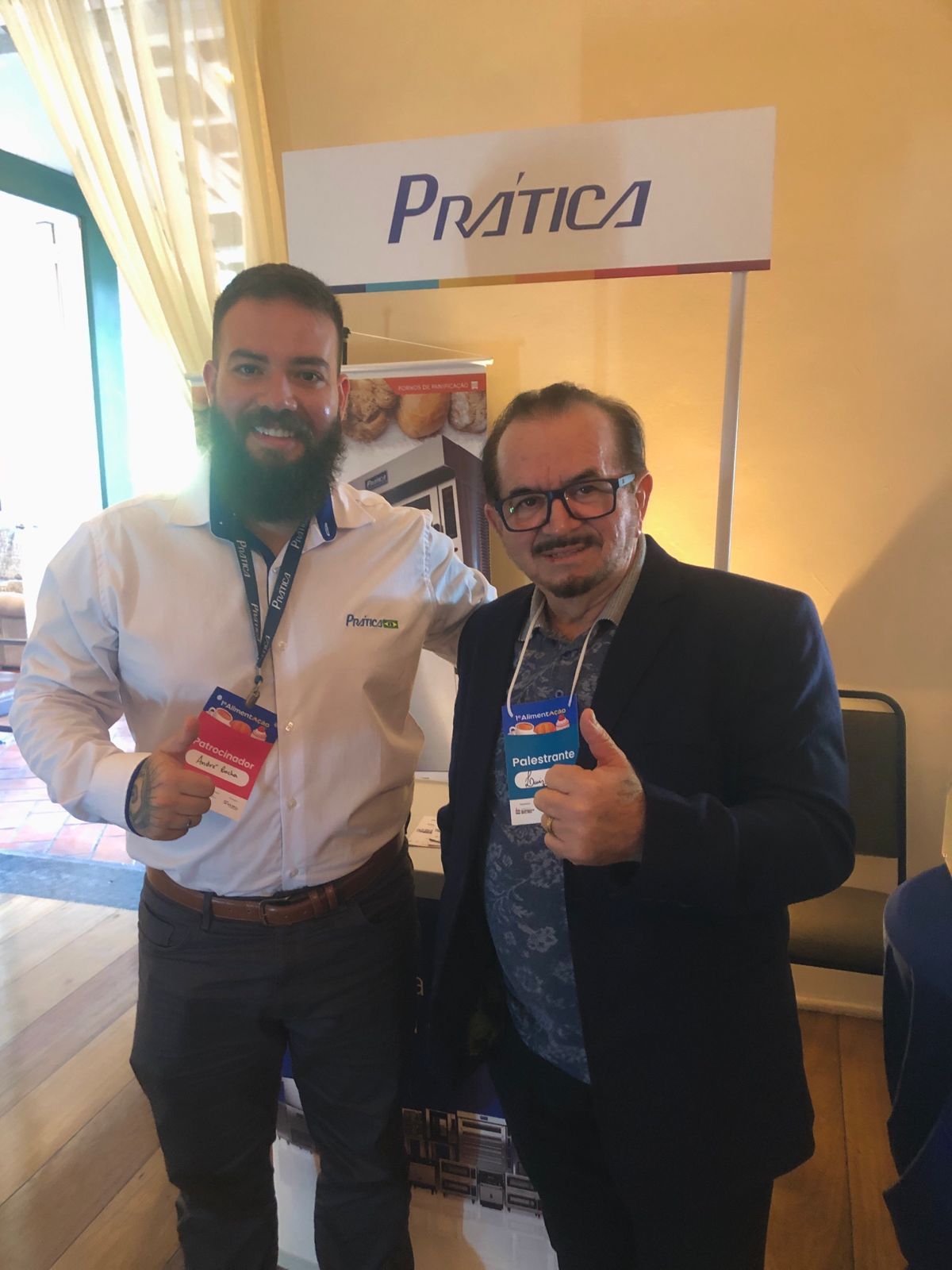 Dois homens estão posando para uma foto em frente a uma placa de prática.