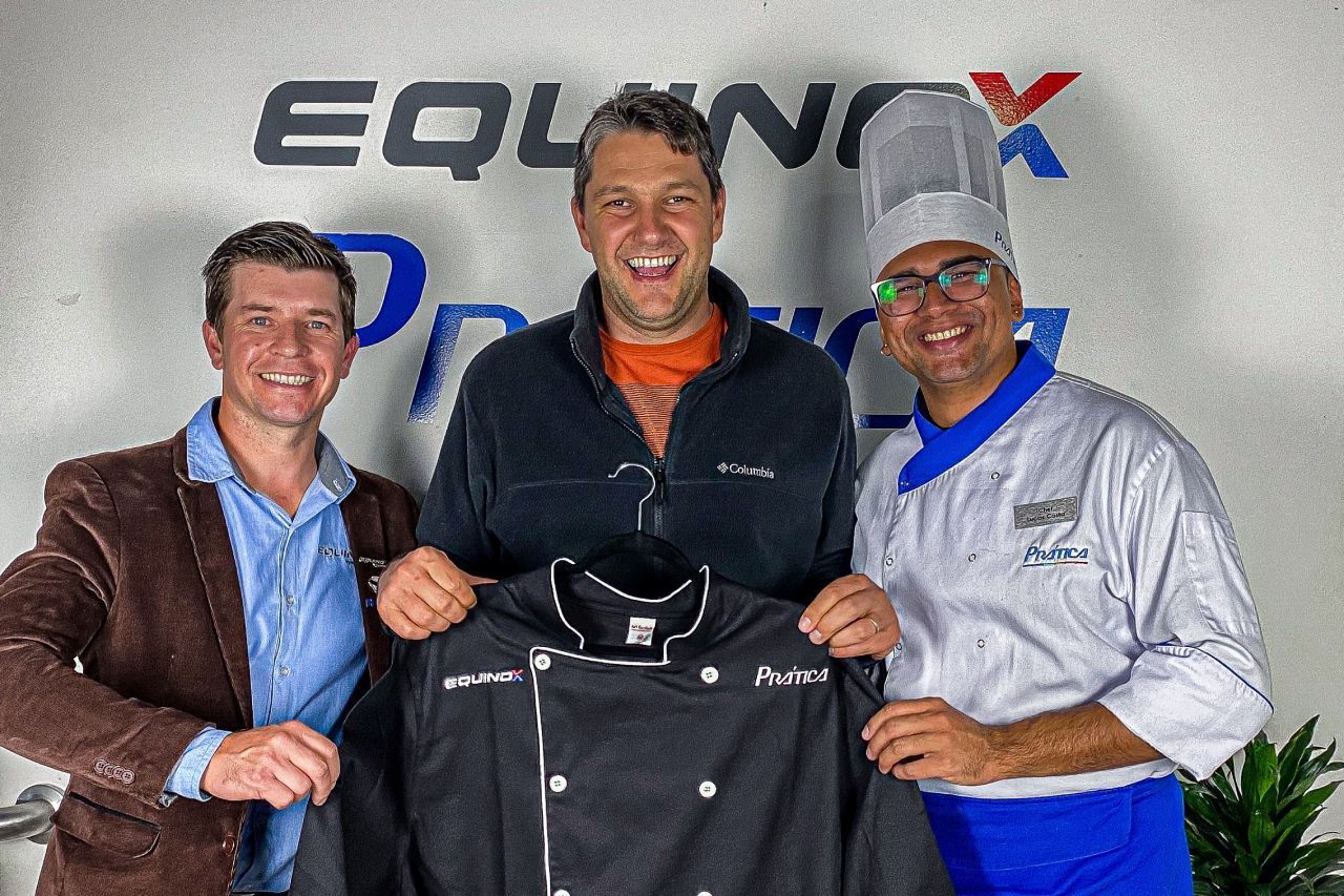 Três homens de pé um ao lado do outro segurando uma jaqueta de chef