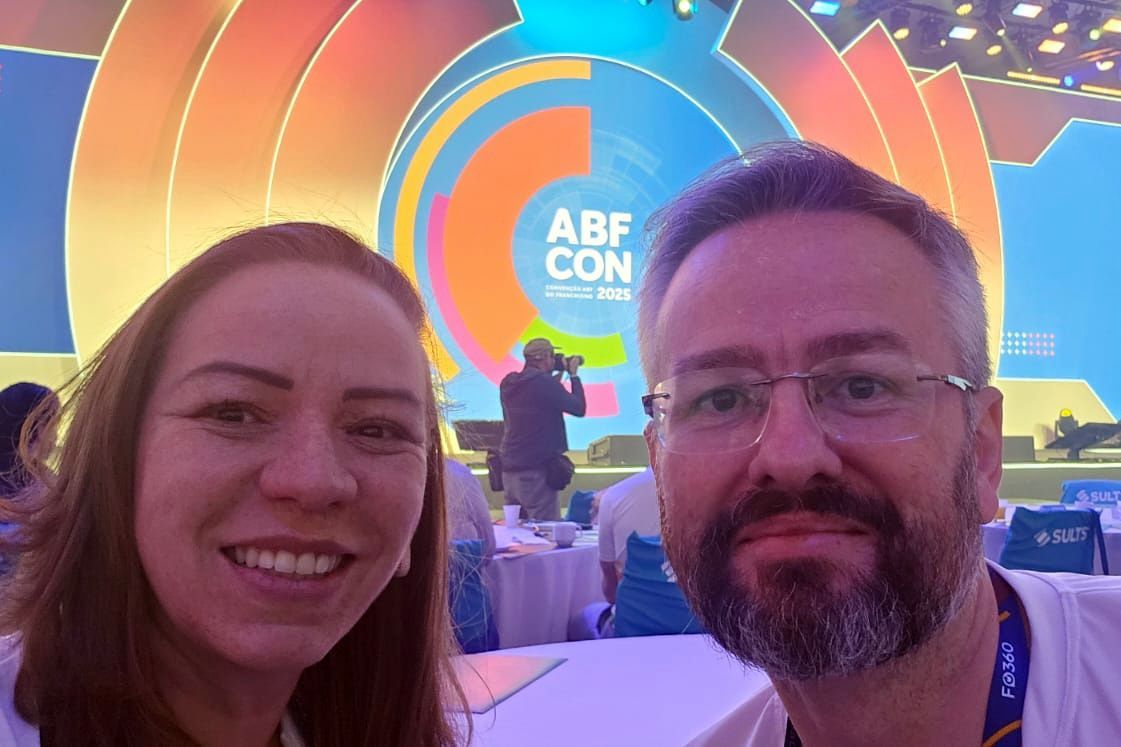 Duas pessoas sorridentes em uma conferência com um logotipo colorido ao fundo.