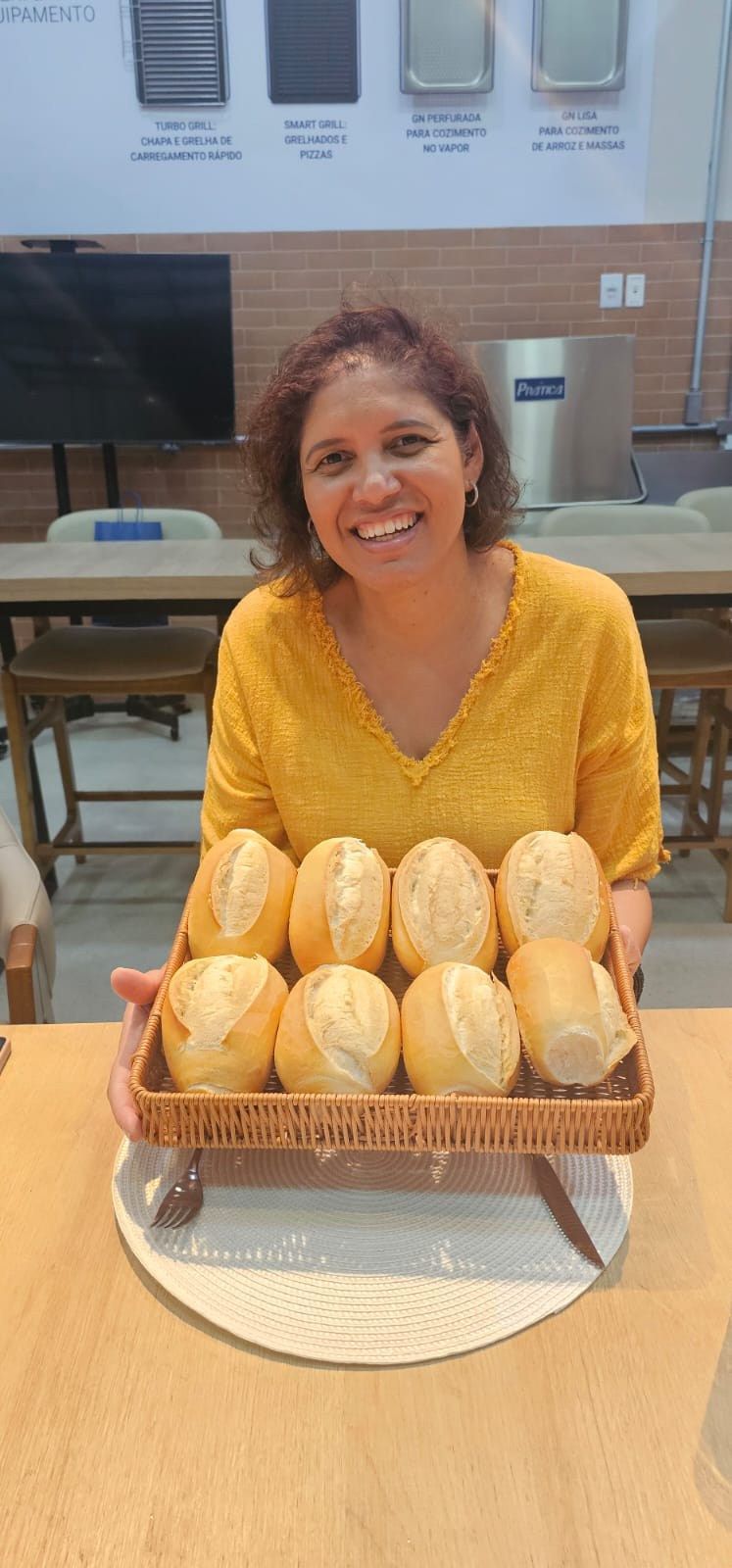 Uma mulher está sentada à mesa segurando uma cesta de pãezinhos.