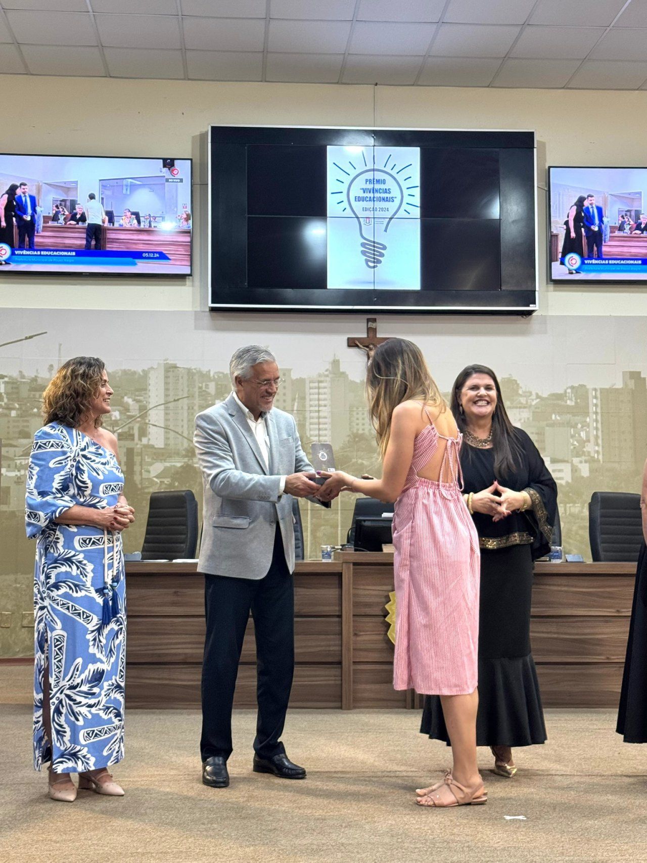 Um grupo de pessoas está em pé em frente a uma tela grande em uma sala.
