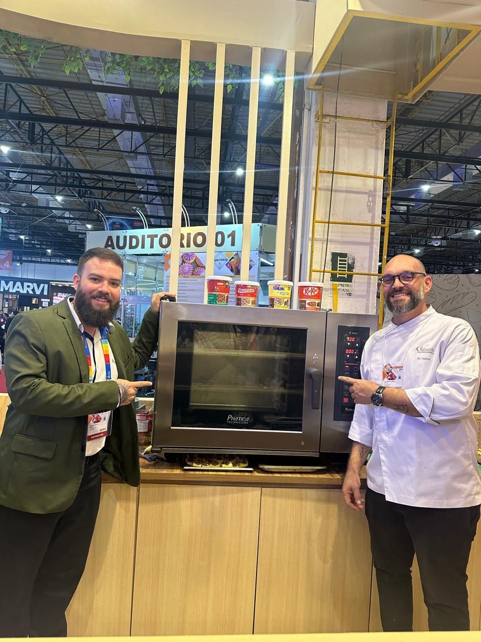 Dois homens estão de pé, um ao lado do outro, em frente a um forno.