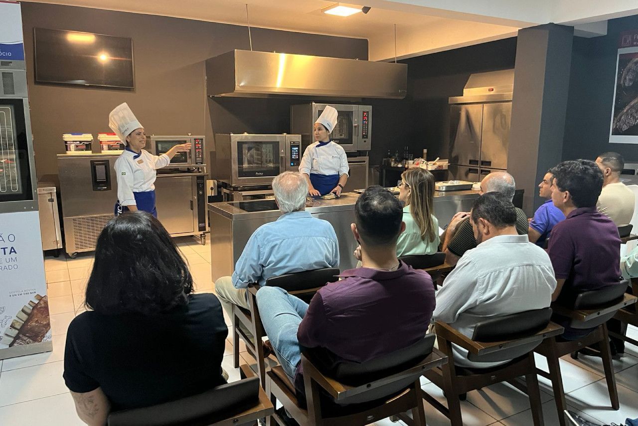 Um grupo de pessoas está sentado em cadeiras em frente a um chef em uma cozinha.