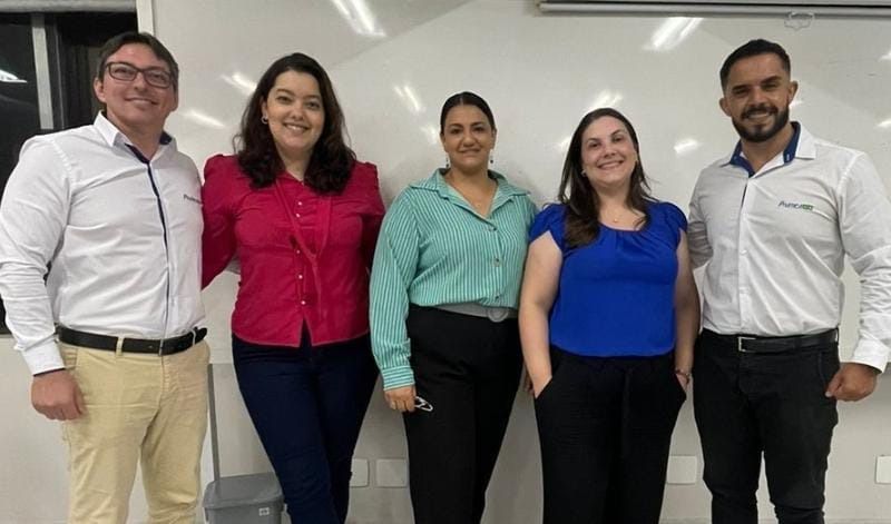 Um grupo de pessoas está posando para uma foto em frente a um quadro branco.