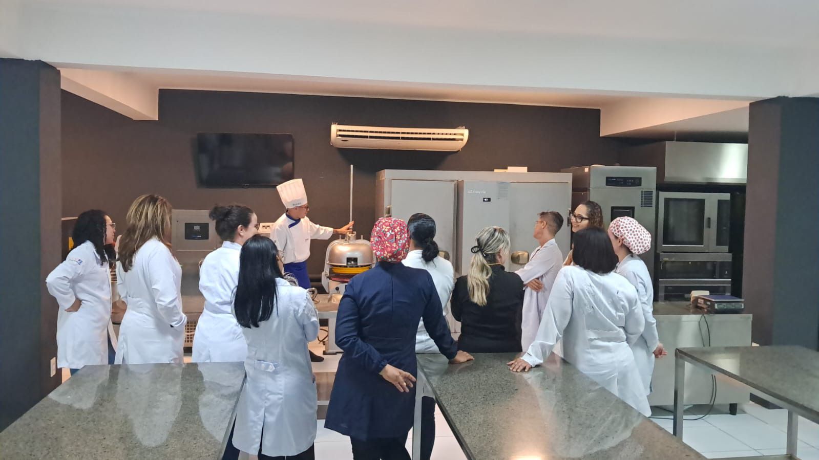 Um grupo de pessoas está em pé ao redor de uma mesa na cozinha.