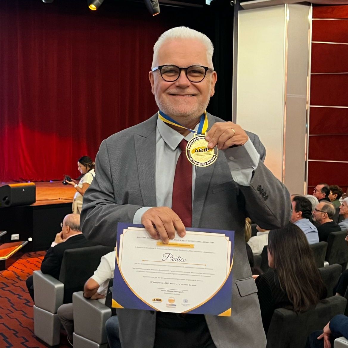 Um homem de terno e gravata segura uma medalha e um certificado