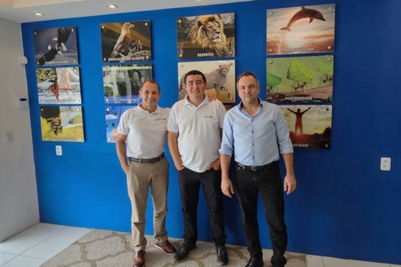Três homens em pé em frente a uma parede azul com fotos
