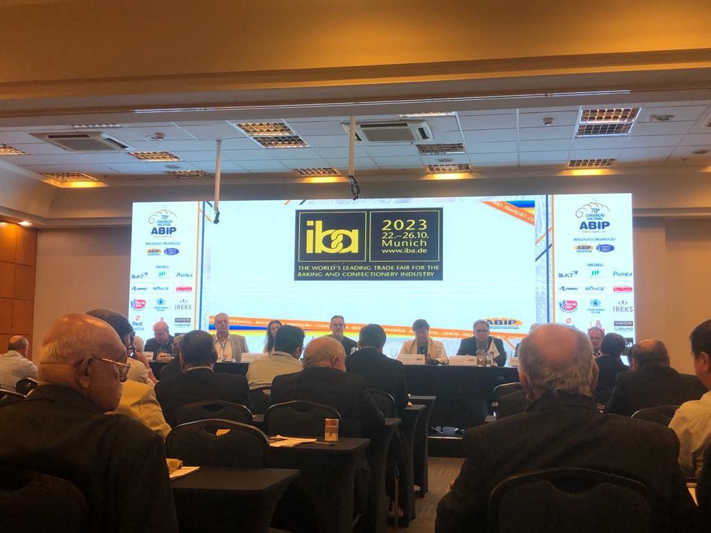 Um grupo de pessoas está sentado em frente a uma tela grande em uma sala de conferências.