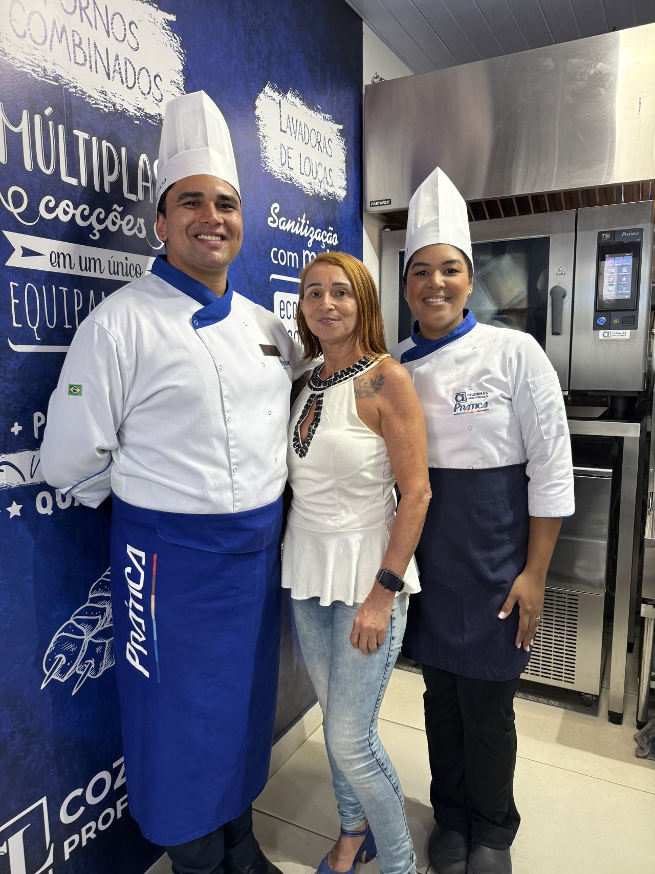 Três chefs estão posando para uma foto com uma mulher na cozinha.