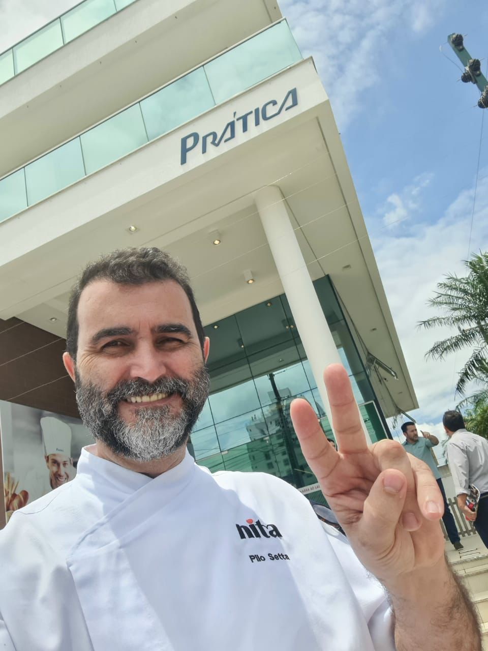 Um homem com barba está parado em frente a um prédio que diz pratica
