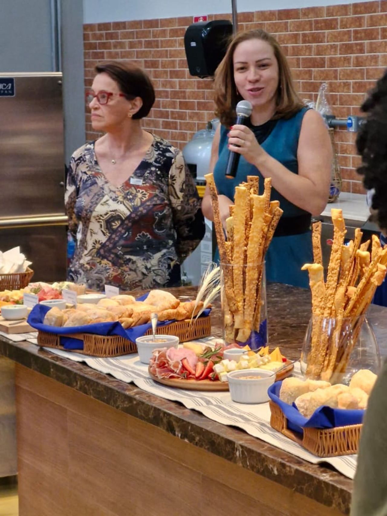 Uma mulher segura um microfone em frente a uma mesa cheia de comida.