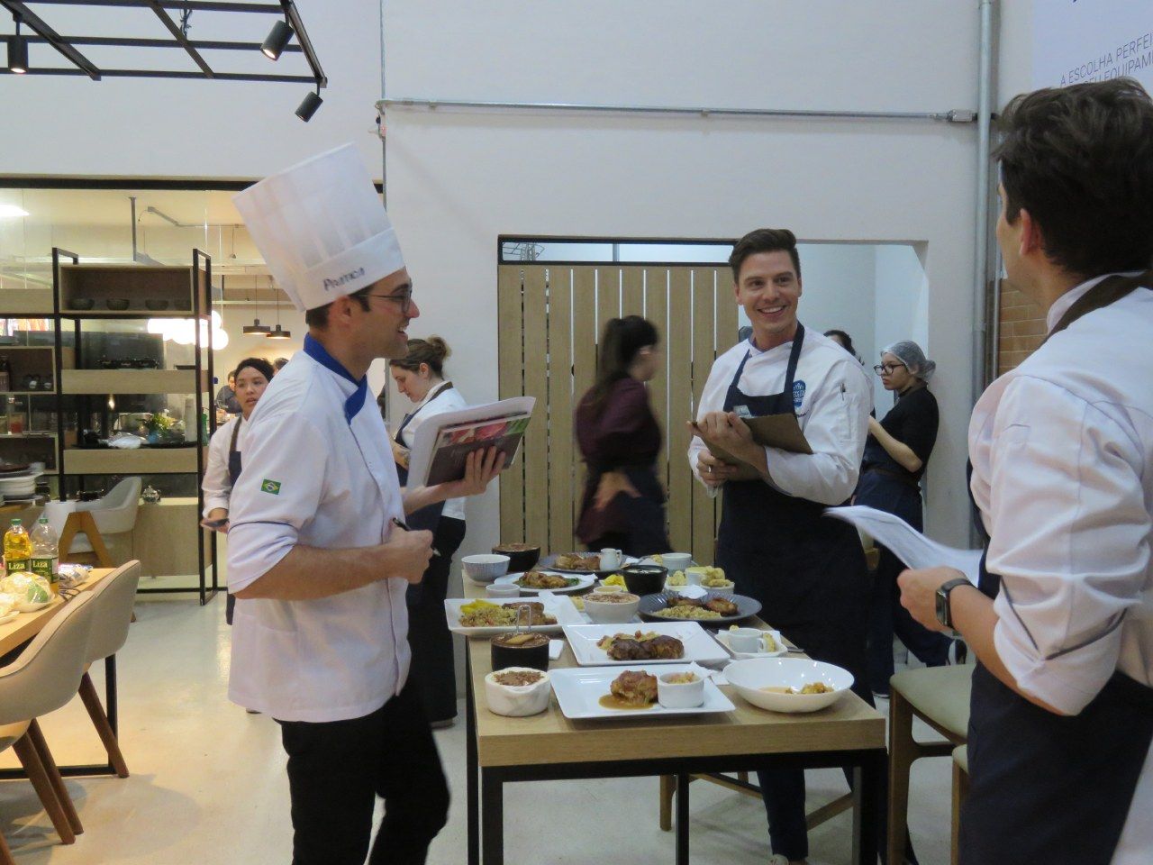 Um grupo de chefs estão em volta de uma mesa com pratos de comida
