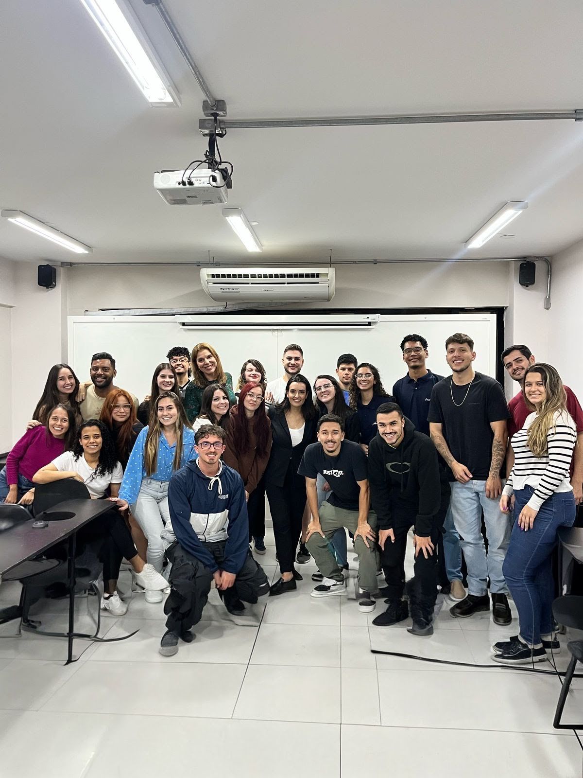 Um grupo de pessoas está posando para uma foto em uma sala de aula.