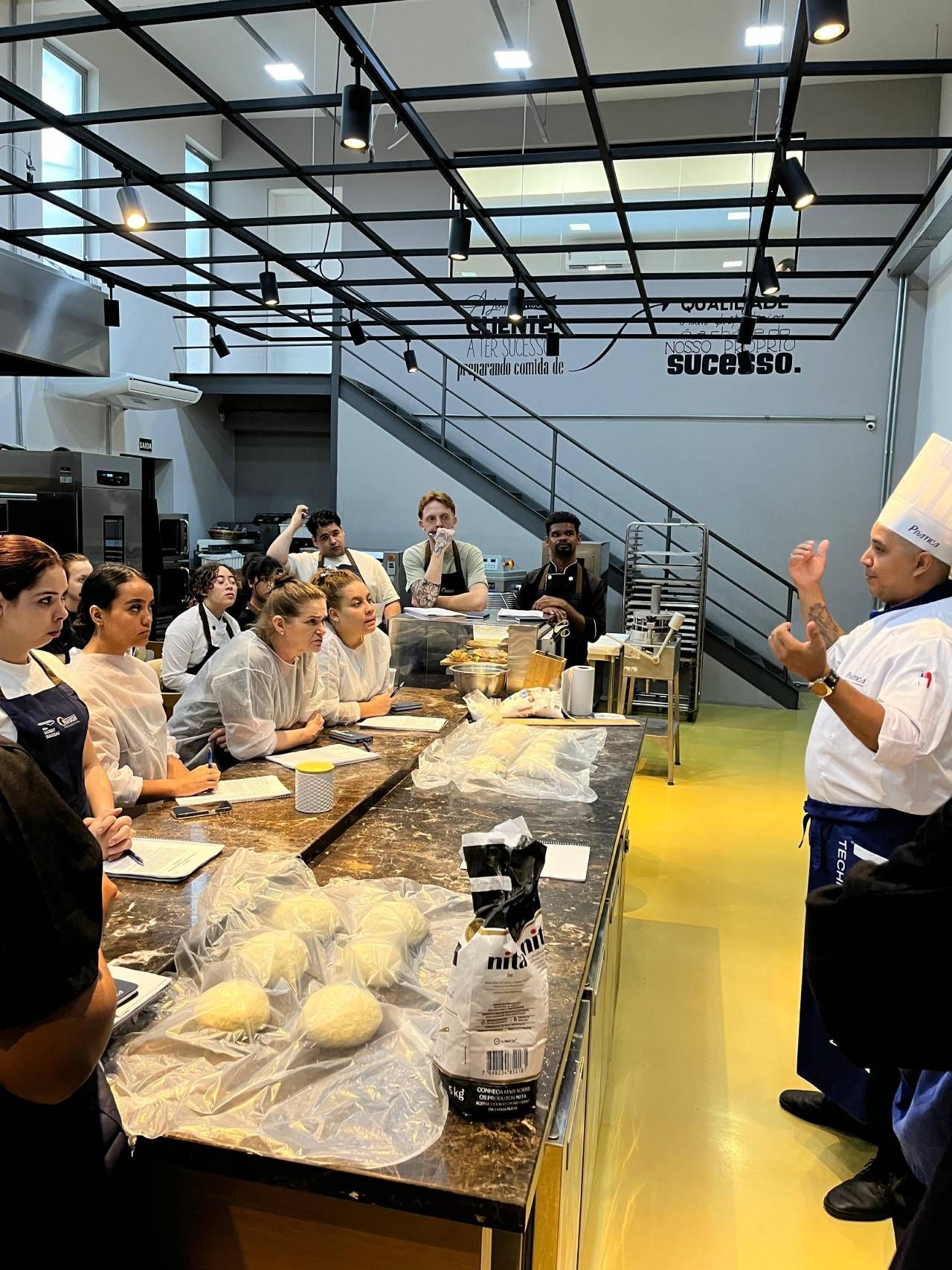 Um chef está fazendo uma apresentação para um grupo de pessoas em uma cozinha.