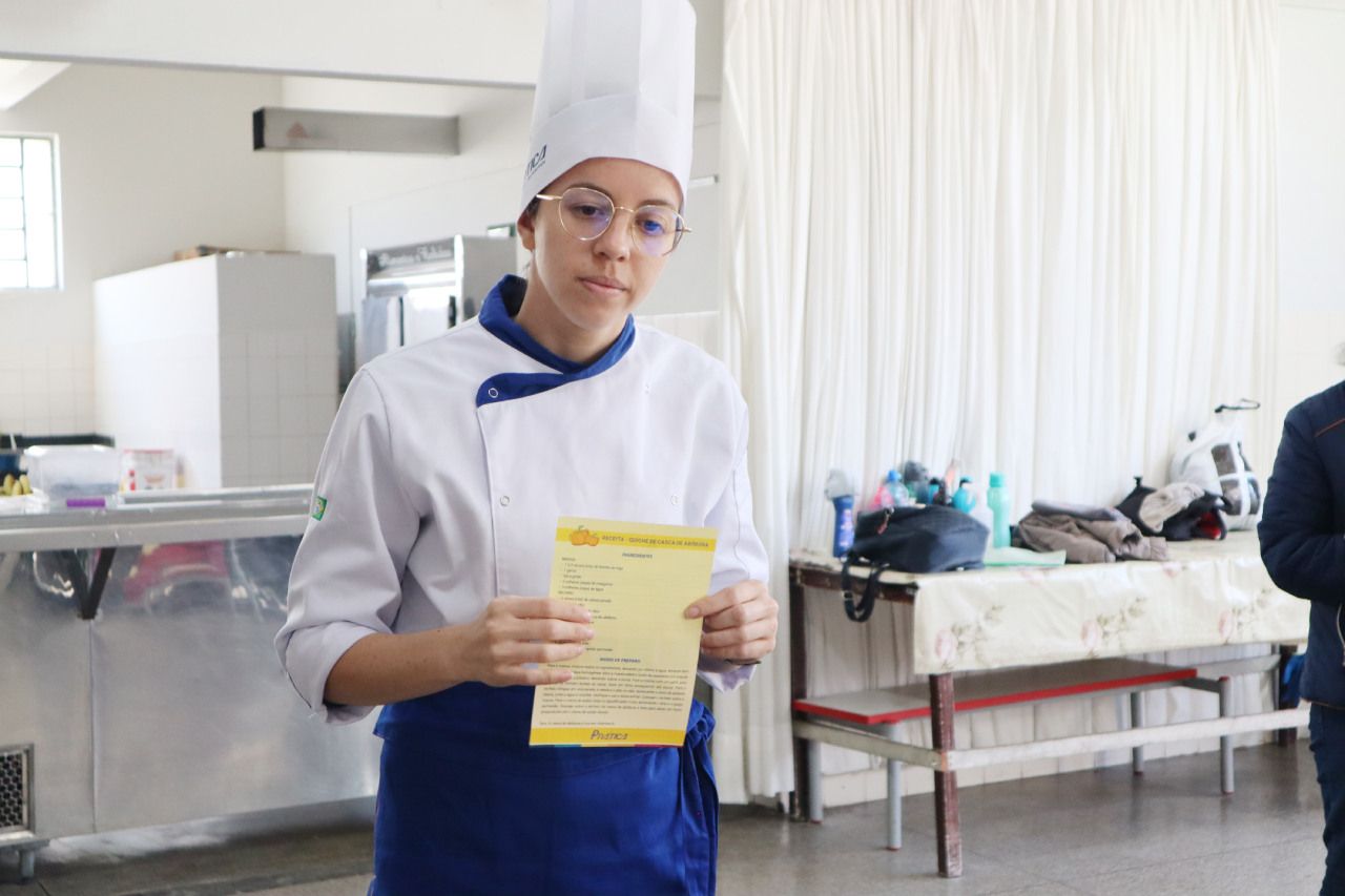 Uma mulher com um chapéu de chef está segurando um pedaço de papel em uma cozinha.