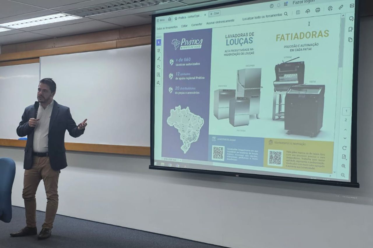 Um homem está fazendo uma apresentação em frente a uma tela grande em uma sala de aula.