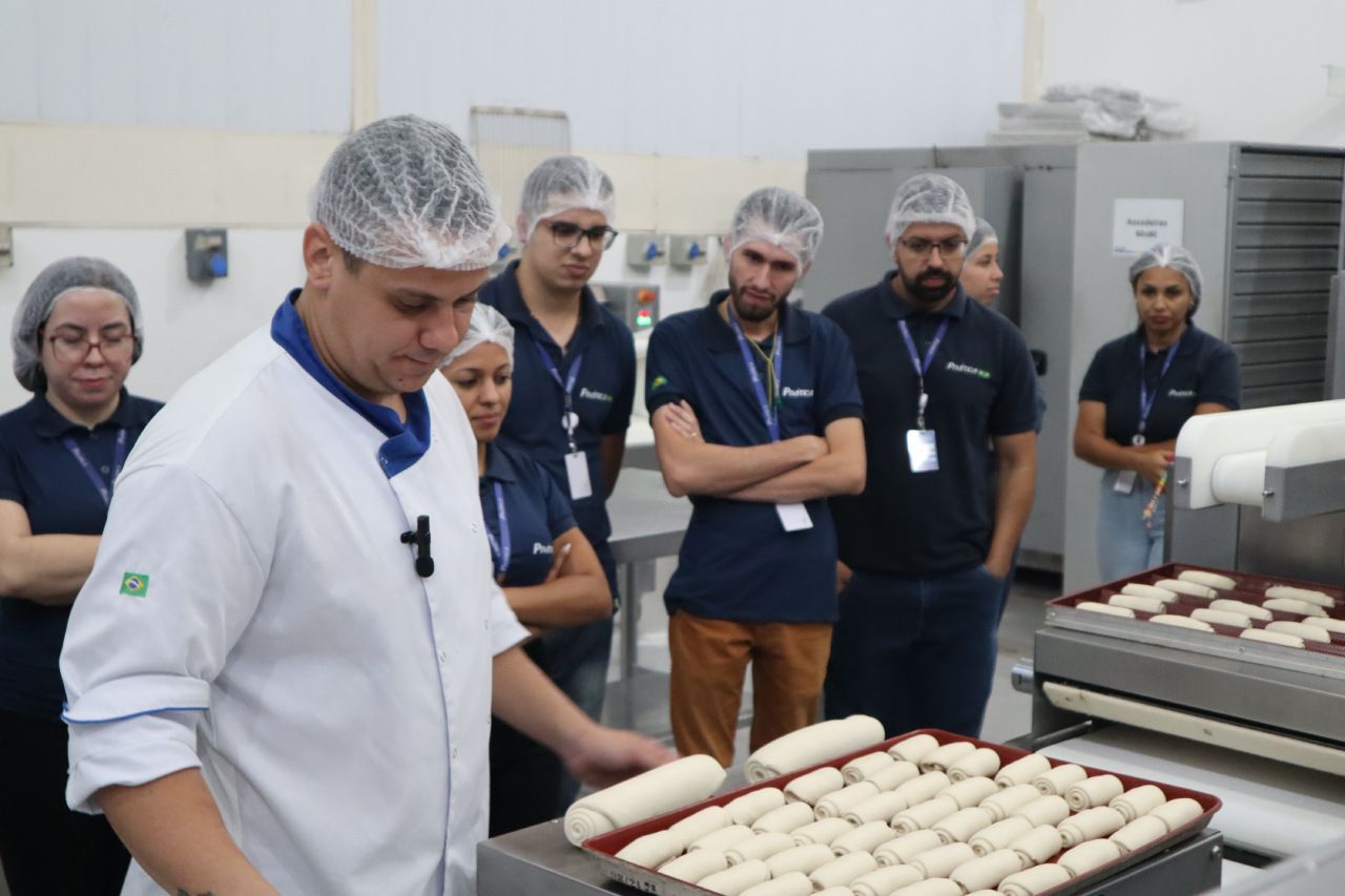 Um grupo de pessoas está em pé ao redor de uma bandeja de comida.