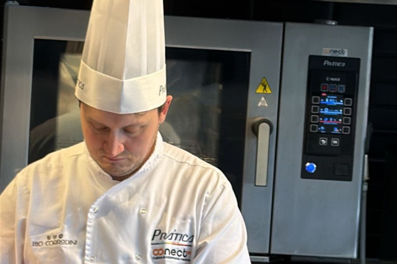 Chef de uniforme branco e touca, trabalhando perto de um forno comercial.