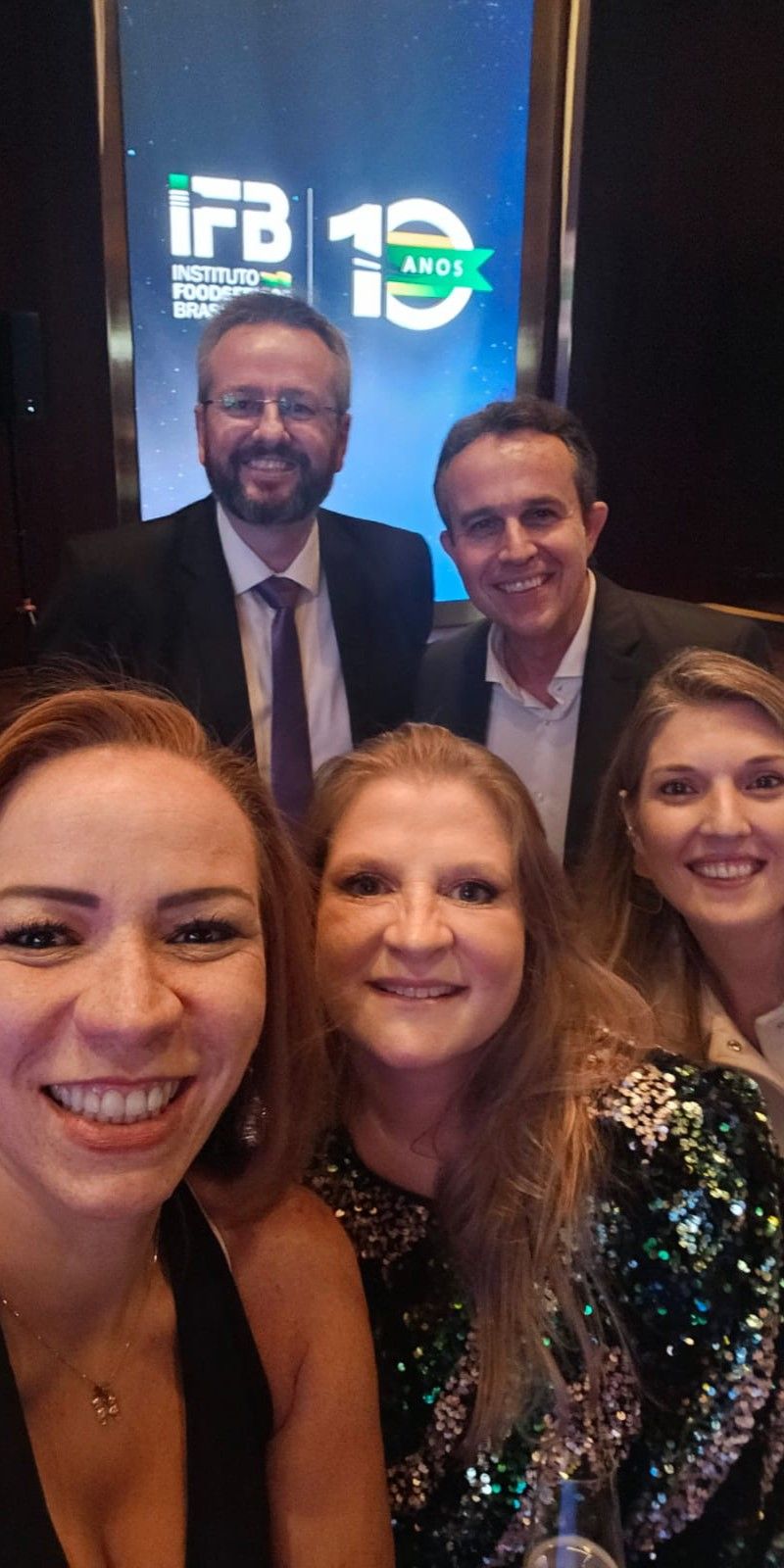 Um grupo de pessoas está posando para uma foto em frente a uma tela.