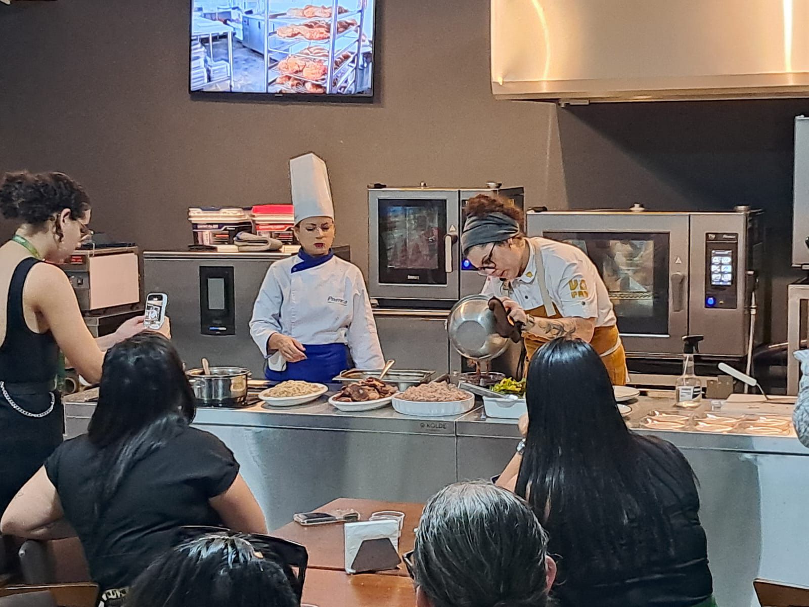 Um grupo de pessoas está observando um chef preparando comida em uma cozinha.