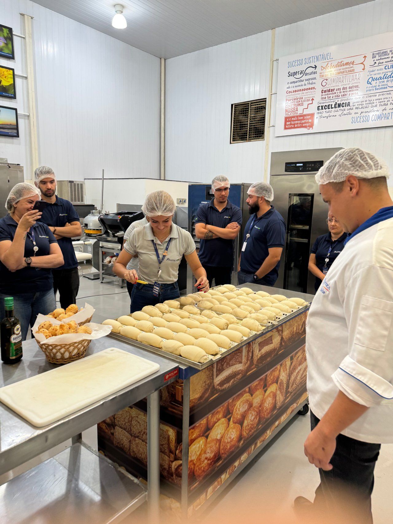 Um grupo de pessoas está em pé ao redor de uma mesa em uma padaria.