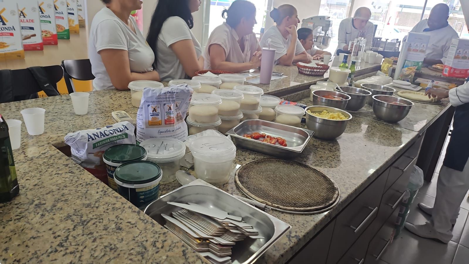 Um grupo de pessoas está sentado à mesa em uma cozinha preparando comida.