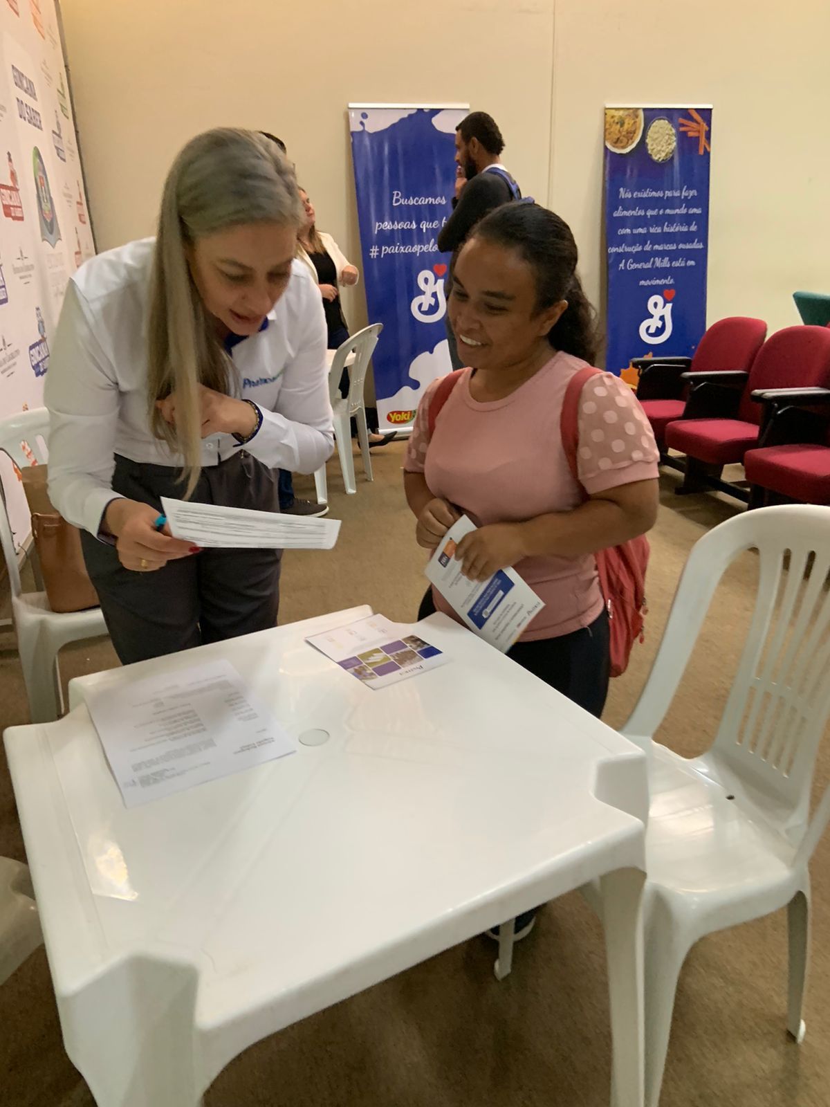 Duas mulheres estão sentadas à mesa olhando papéis.