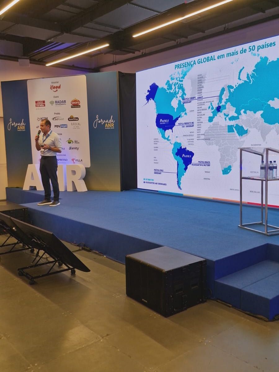 Um homem está em pé em um palco em frente a uma tela grande com um mapa do mundo nela