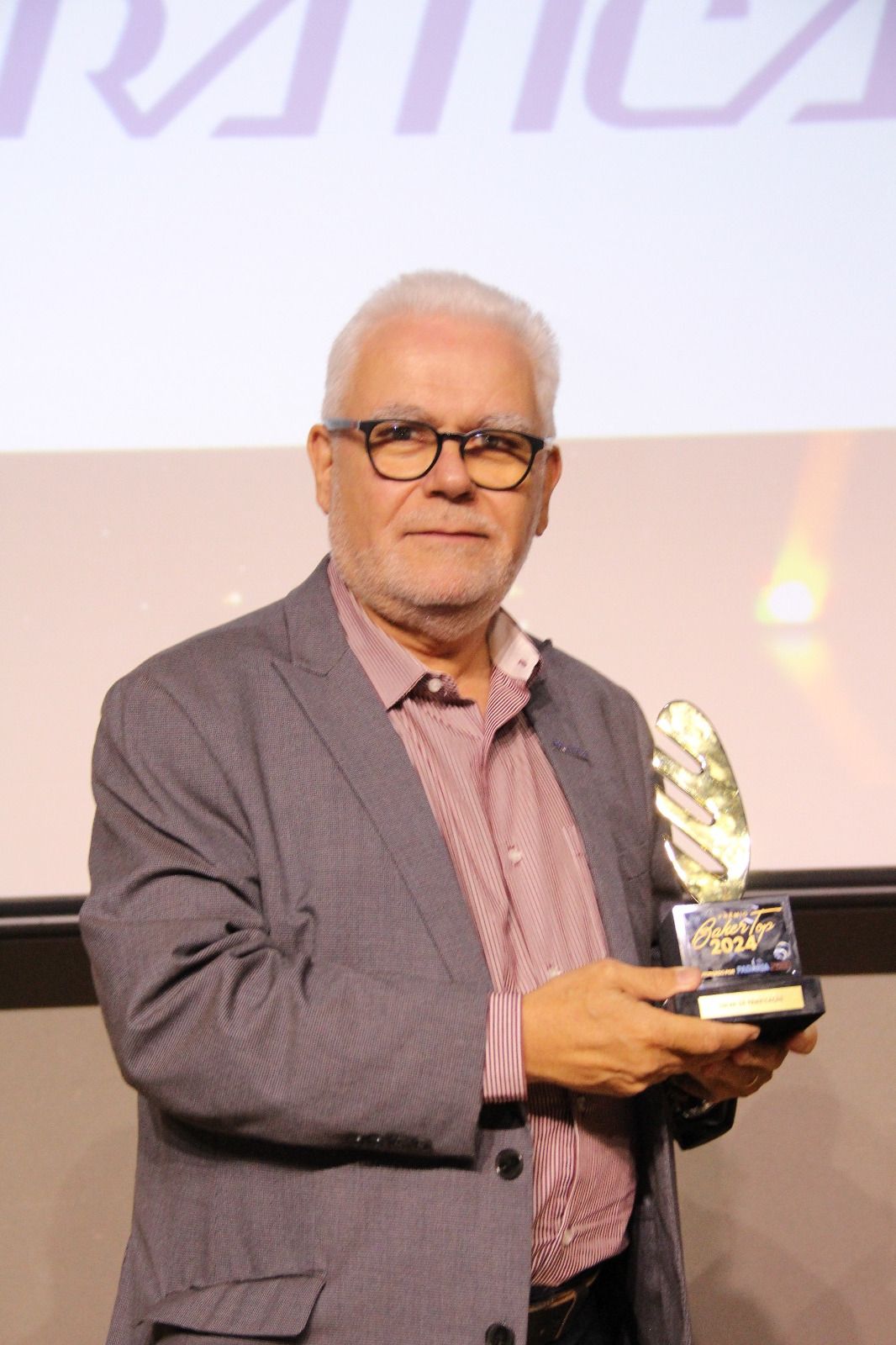 Um homem de terno e óculos está segurando um troféu