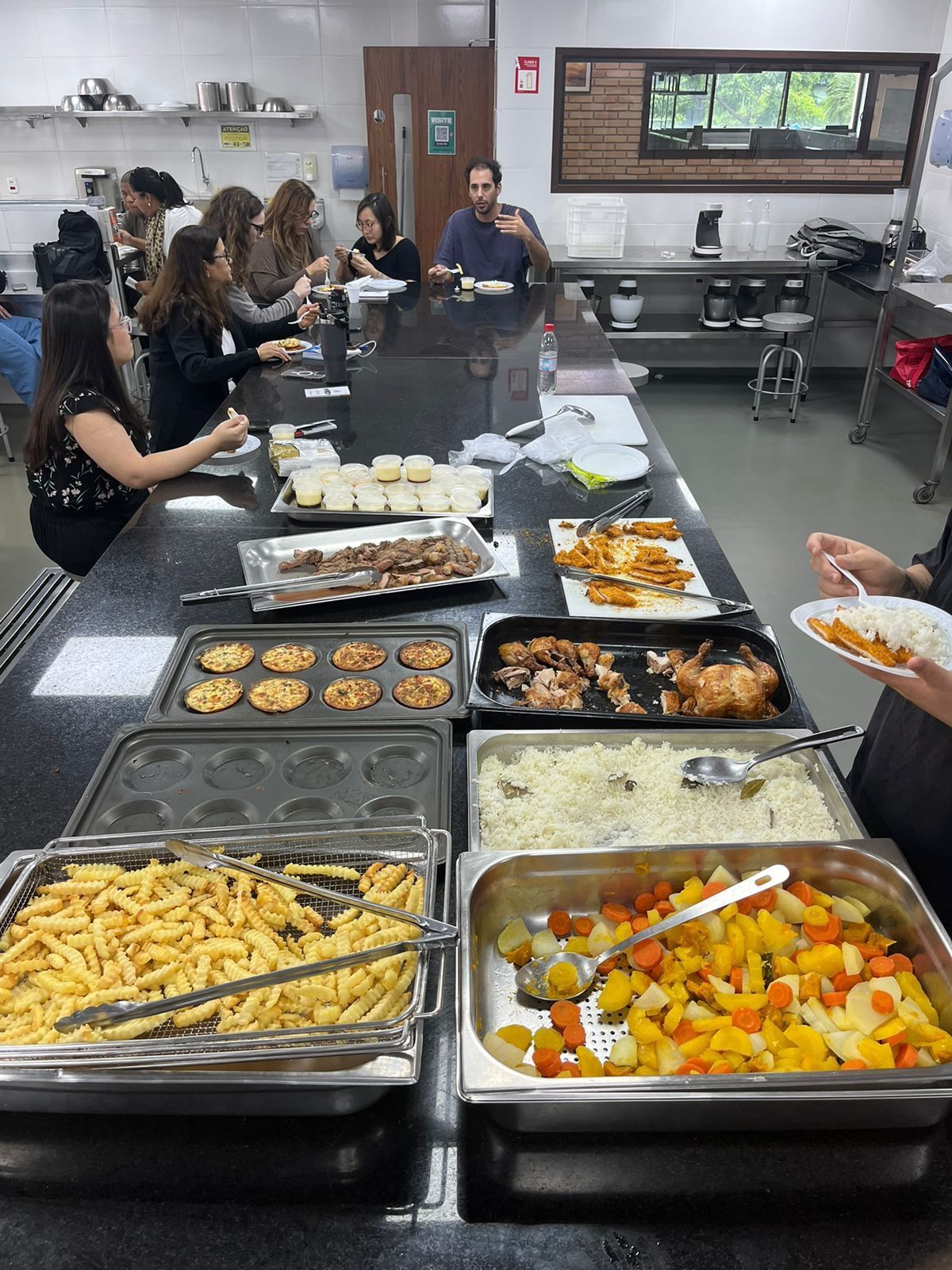 Um grupo de pessoas está sentado à mesa comendo comida de um bufê.