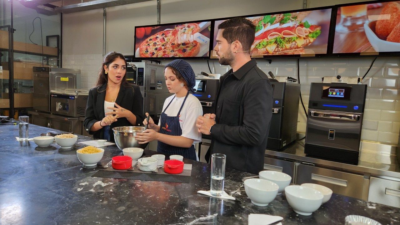 Um grupo de pessoas está em pé ao redor de uma mesa em uma cozinha preparando comida.
