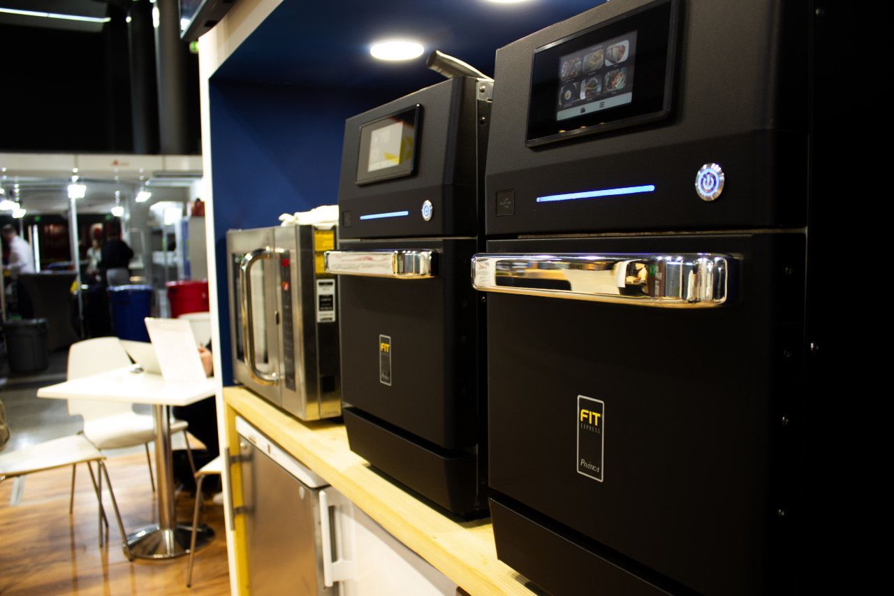 Uma fileira de aparelhos pretos estão alinhados em uma mesa de madeira