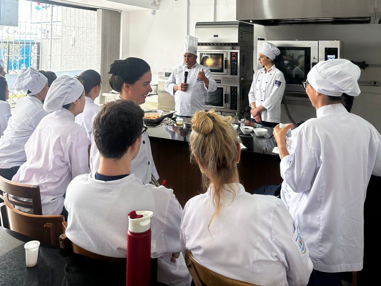 Um grupo de pessoas está sentado ao redor de uma mesa observando um chef
