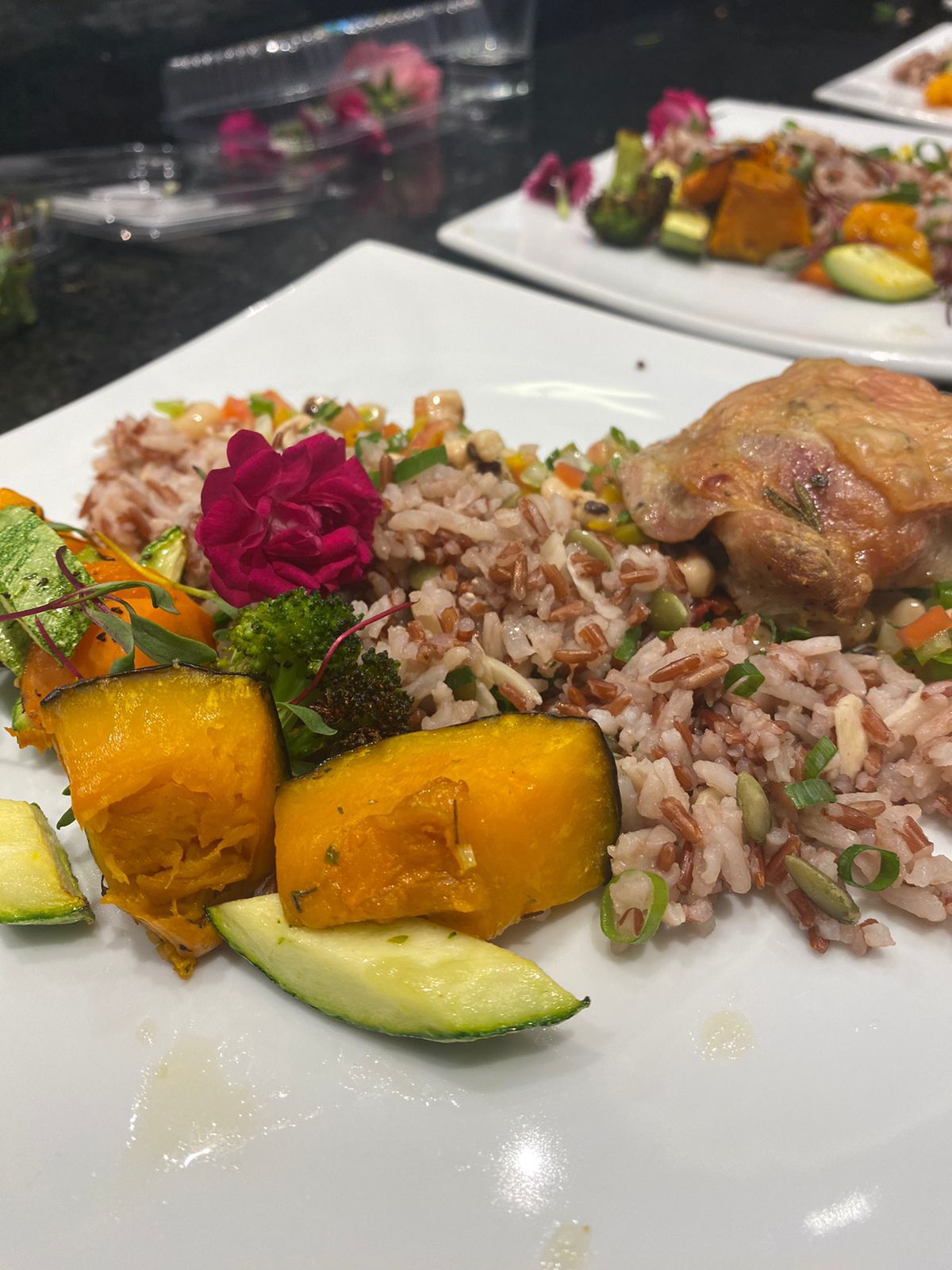 Um close de um prato de comida com arroz, vegetais e flores sobre uma mesa.