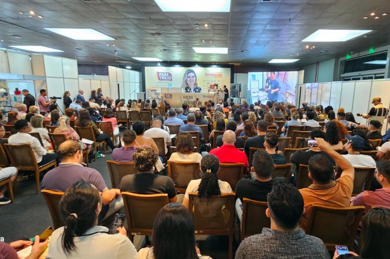 Um grande grupo de pessoas está sentado em cadeiras em uma sala de conferências.