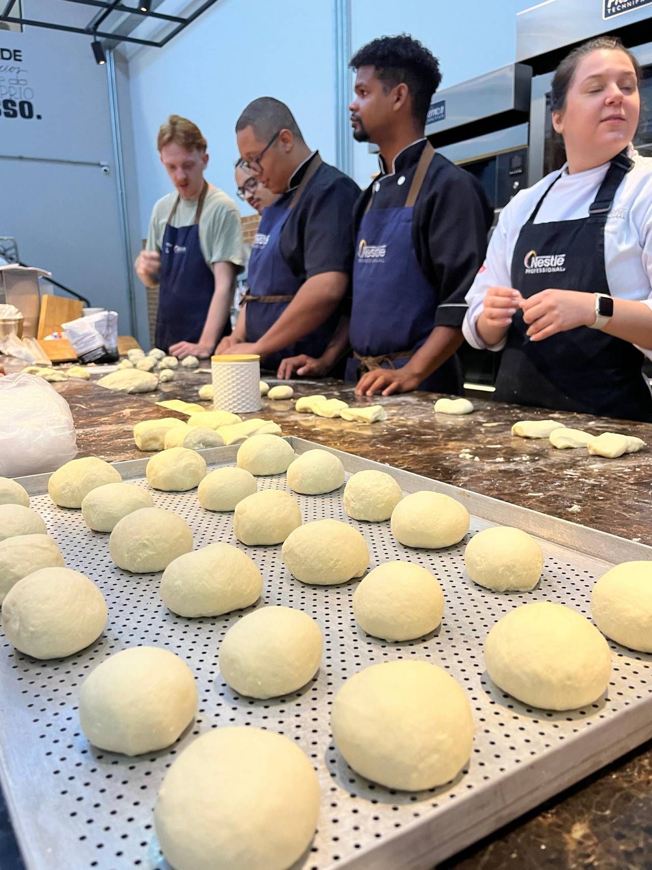 Um grupo de pessoas está em pé ao redor de uma mesa com massa sobre ela.