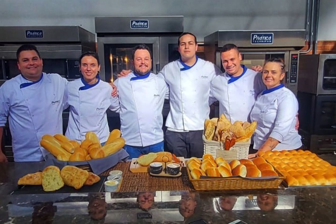 Um grupo de chefs está posando para uma foto em frente a uma mesa cheia de pão.