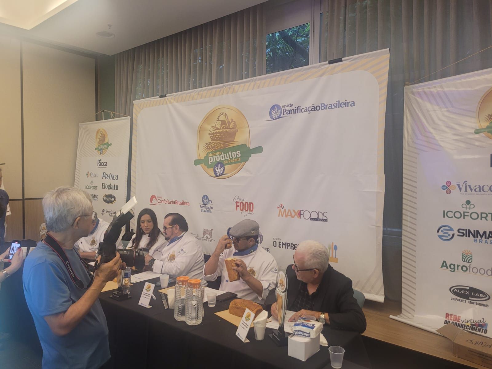 Um grupo de pessoas está sentado em uma mesa em frente a uma grande faixa.