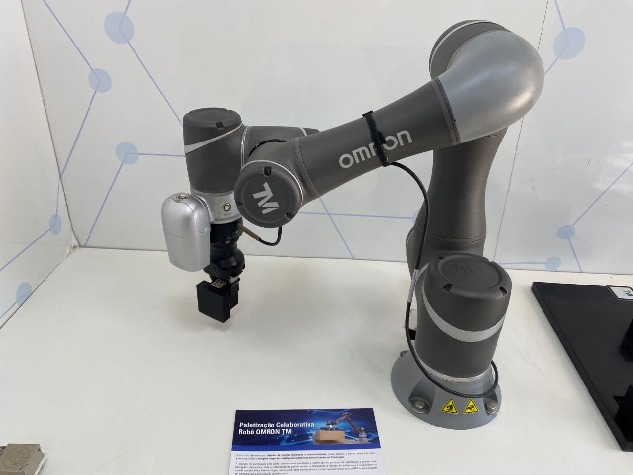 Um braço robótico está sobre uma mesa ao lado de um cartão de visita.