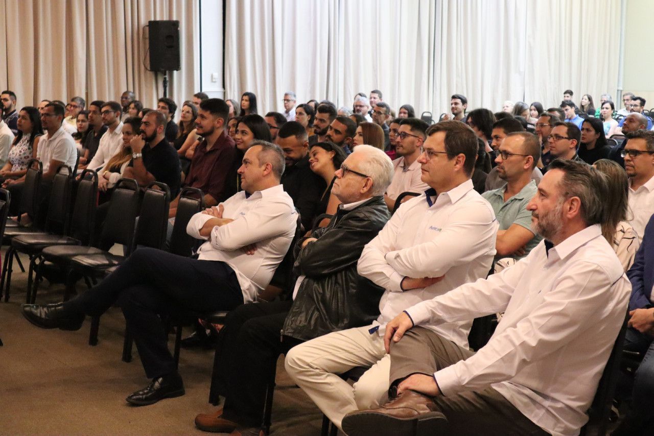 Um grande grupo de pessoas está sentado em cadeiras em uma sala.