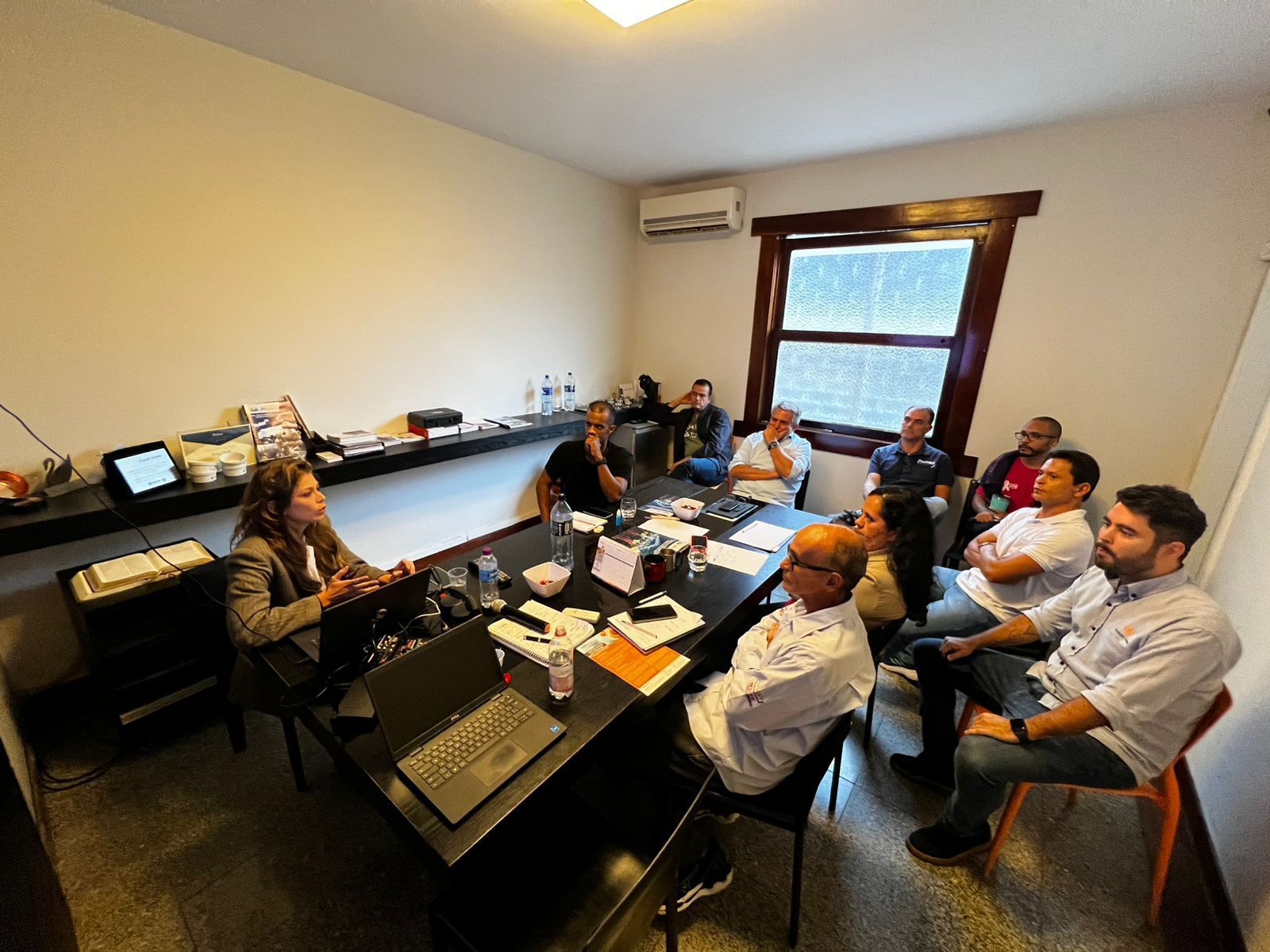 Um grupo de pessoas está sentado ao redor de uma mesa em uma sala.