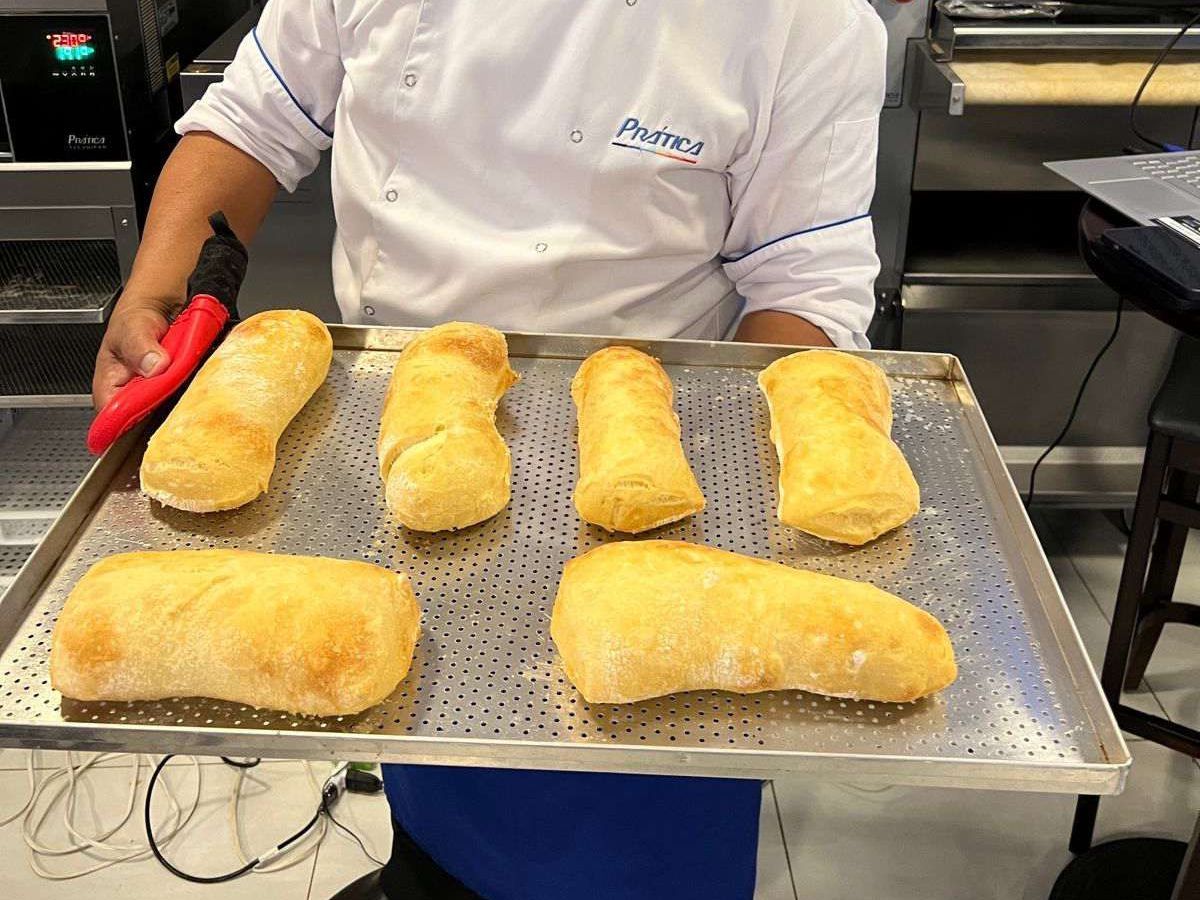 Um chef está segurando uma bandeja de pão na cozinha.