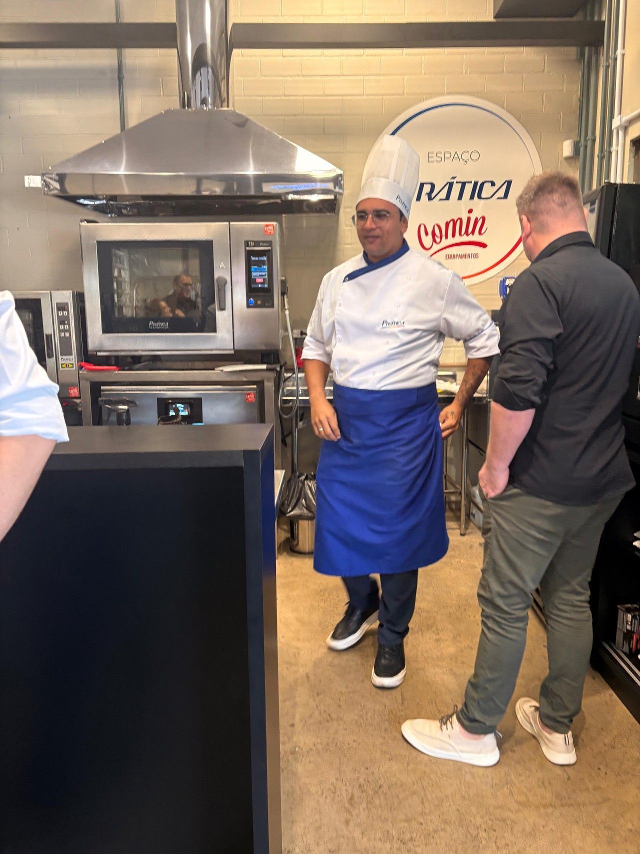 Dois homens estão em uma cozinha conversando com um chef.